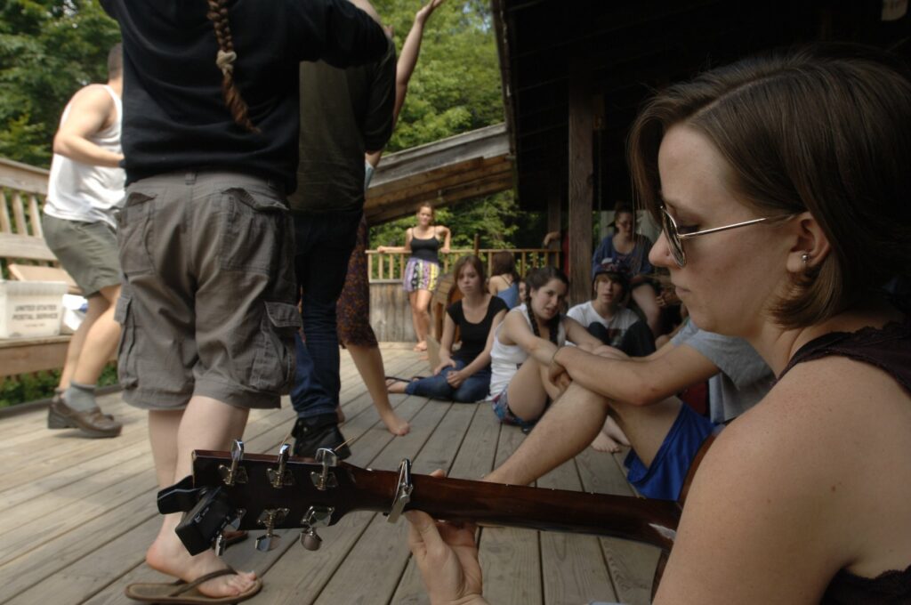 Campers relaxing on the porch with a guitar at Rowe Camp