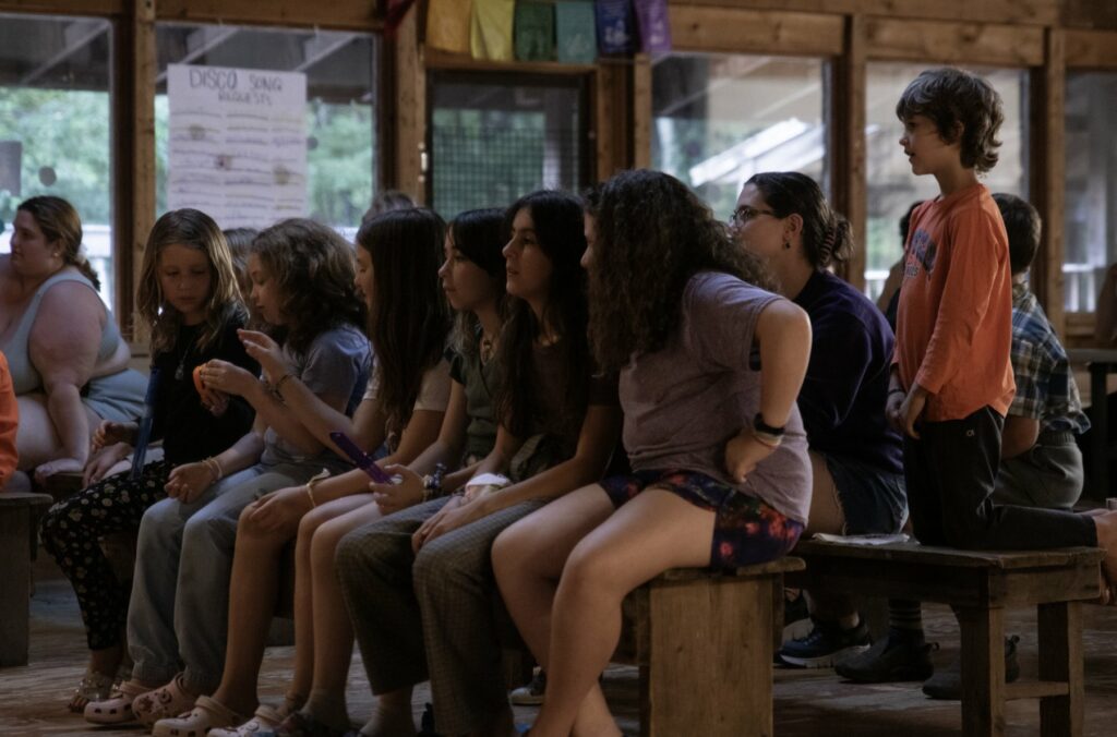 Campers sitting together on benches in the Rec Hall at Rowe Camp